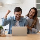 Family standing in domestic kitchen reading e-mail from bank on laptop celebrate loan mortgage approval, happy couple of lottery victory, great commercial offer, e-commerce sale and discount concept